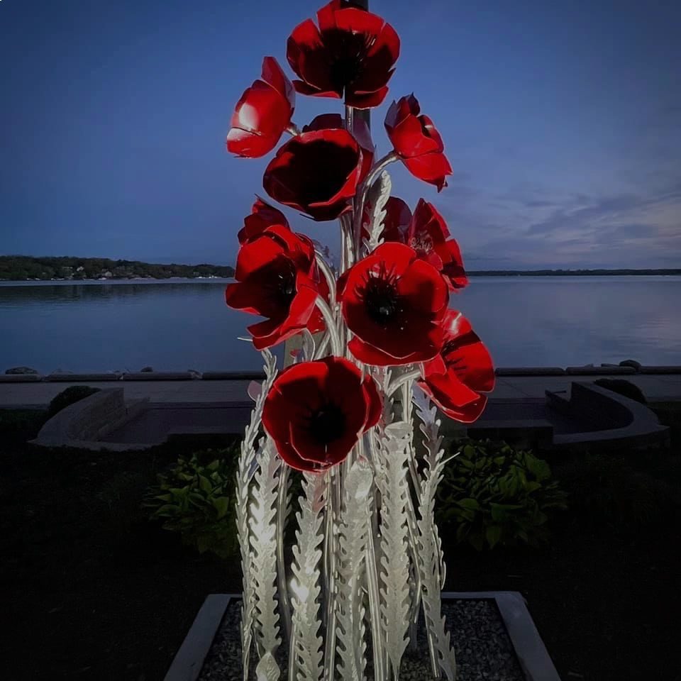 A red flower sculpture in front of water.