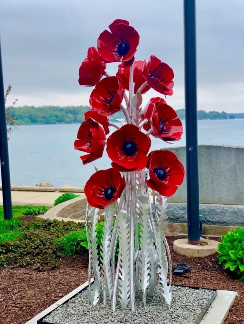 A glass sculpture of red flowers in front of water.