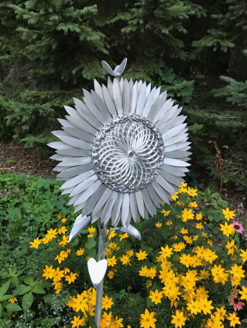 A metal sculpture of a sunflower in the middle of some flowers.