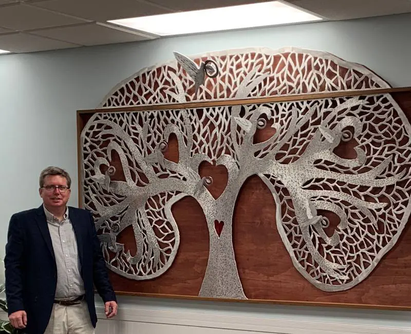 A man standing in front of a large wooden tree.